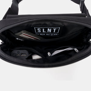 Minimalist black Faraday sling bag by SLNT, featuring RFID-blocking technology, a spacious main compartment filled with a wallet and tech accessories