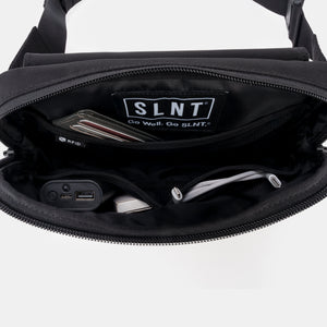 Minimalist black Faraday sling bag by SLNT, featuring RFID-blocking technology, a spacious main compartment filled with a wallet and tech accessories