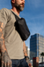 A man with tattooed arms wears a black Faraday bag by SLNT across his chest against a city skyline. The sling bag features a built-in Faraday cage for signal blocking.